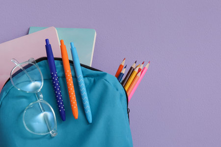 Blue school backpack with different stationery and eyeglasses on purple backgroundの写真素材