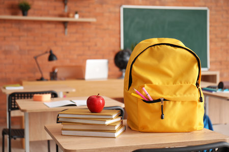 Backpack with fresh apple and books on desk in classroomの写真素材