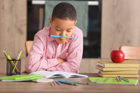Funny little African-American boy doing homework in the kitchen