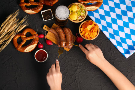 Woman eating tasty Bavarian sausages on black background.  celebrationの写真素材