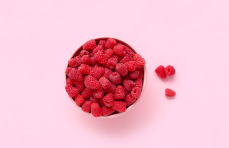 Bowl with fresh raspberry on pink background