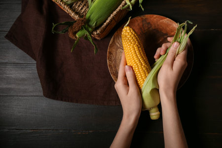 Woman peeling corn cob on black wooden table