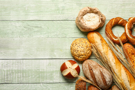 Different types of bread, bag of flour and wheat ears on green wooden tableの写真素材