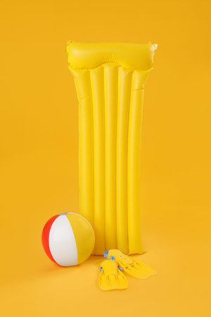 Inflatable mattress with beach ball and flippers on yellow backgroundの写真素材