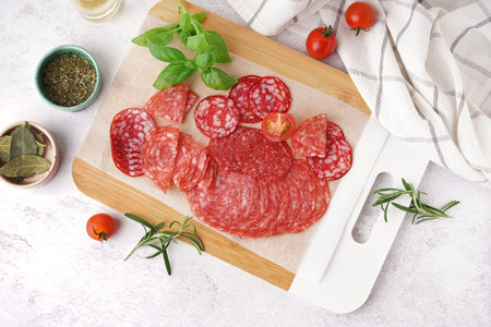 Wooden board with slices of tasty salami on light background