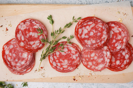 Wooden board with slices of tasty salami on light background