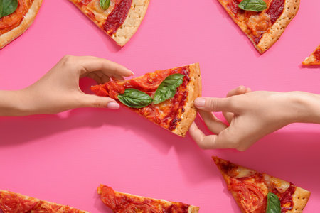 Women holding slice of tasty pizza on pink backgroundの写真素材