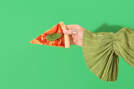 Woman holding slice of tasty pizza on green background