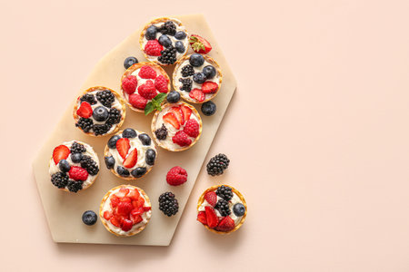Board of tasty tartlets with whipped cream and berries on beige backgroundの写真素材