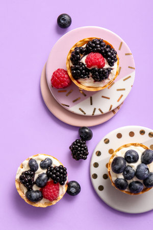 Tasty tartlets with whipped cream and berries on lilac backgroundの写真素材