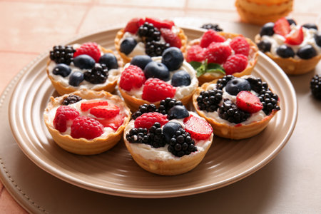 Plate of tasty tartlets with whipped cream and berries on pink tile backgroundの写真素材