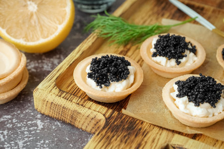 Wooden board of tasty tartlets with black caviar on gray backgroundの写真素材