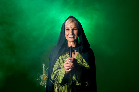 Mature witch with burning candle on dark green backgroundの写真素材