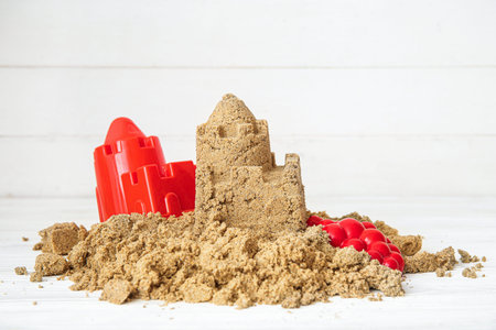 Castle made of sand with beach toys on white wooden background