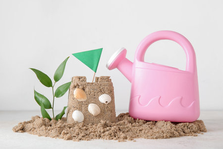 Castle made of sand with watering can and seashells on white background