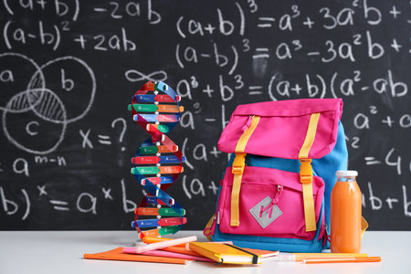 Pink school backpack with stationery, molecular model and bottle of juice on white table near black...