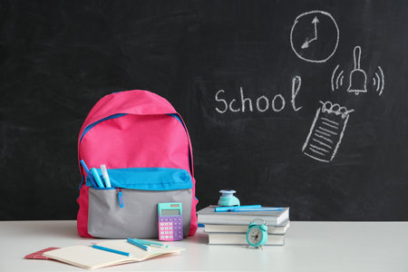 Colorful school backpack with different stationery on white table near black chalkboardの写真素材