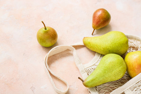 Mesh bag with ripe pears on pink table