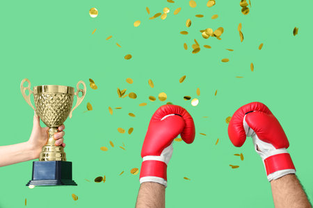 Female hand with gold cup, male hands in boxing gloves and confetti on green backgroundの写真素材