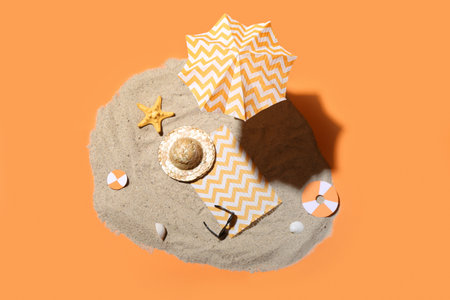 Creative summer composition with mini umbrella, beach accessories and sand on orange backgroundの写真素材