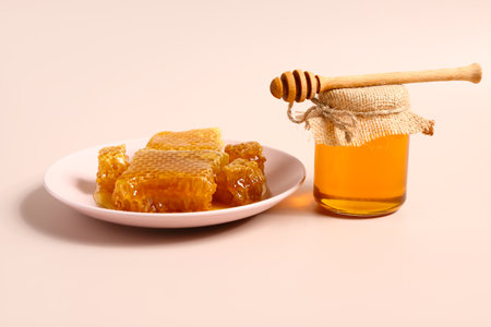Jar of sweet honey and plate with combs on pink backgroundの写真素材