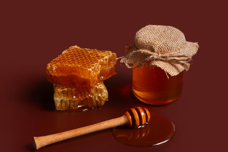 Jar of sweet honey with combs and dipper on red backgroundの写真素材