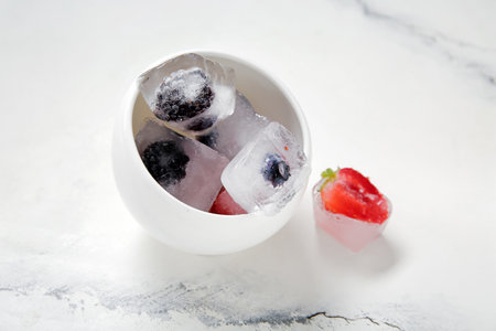 Bowl with frozen berries in ice cubes on white backgroundの写真素材