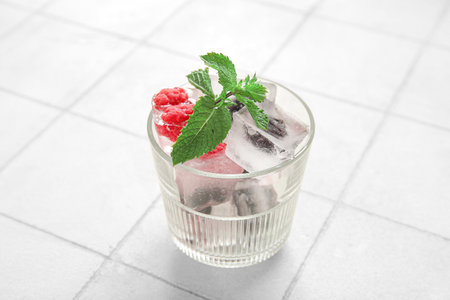Glass with frozen berries in ice cubes and mint on white tile backgroundの写真素材
