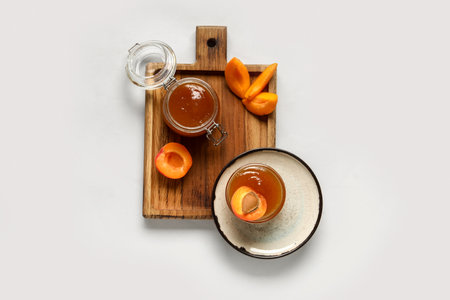 Wooden board with glass bowl and jar of sweet apricot jam on white backgroundの写真素材