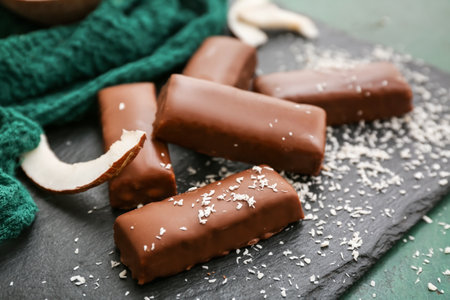 Board with tasty chocolate covered coconut candies on green backgroundの写真素材