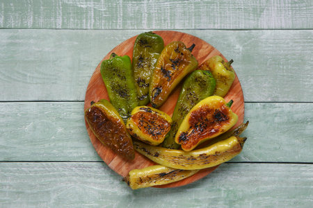 Board with different grilled peppers on green wooden backgroundの写真素材