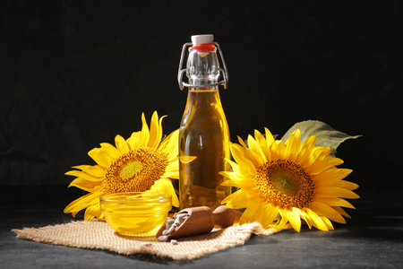 Glass bowl, bottle of sunflower oil and wooden scoop with seeds on black backgroundの写真素材