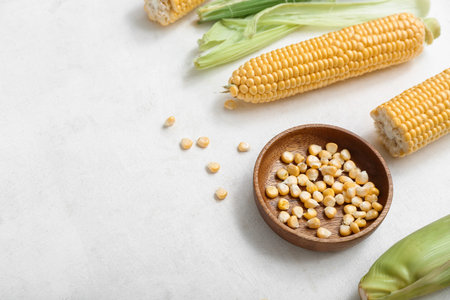Fresh corn cobs and wooden bowl with kernels on white table