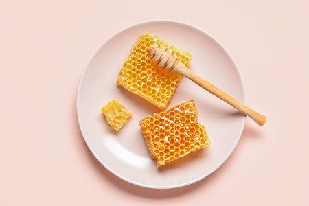 Plate with sweet honeycombs and dipper on pink backgroundの写真素材