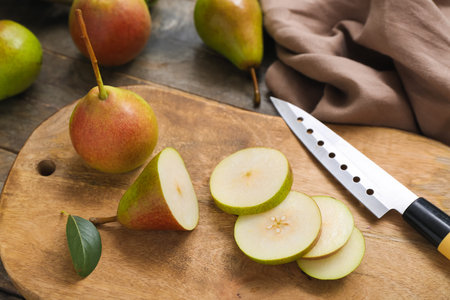Board with sliced pears and knife on gray wooden table, closeup