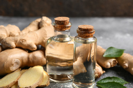 Bottles of ginger cosmetic oil and leaves on gray tableの写真素材