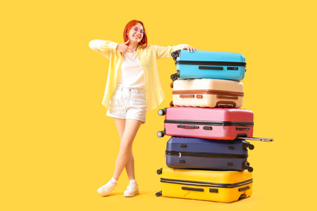 Female tourist with many suitcases on yellow backgroundの写真素材