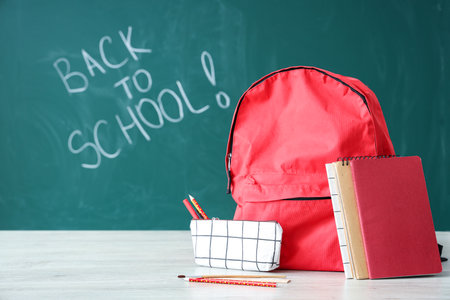 Backpack and supplies on table near green chalkboard with text BACK TO SCHOOLの写真素材