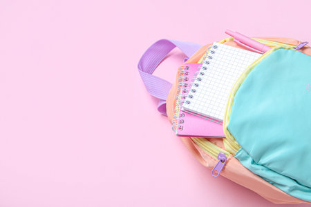 Color school backpack with stationery on pink background