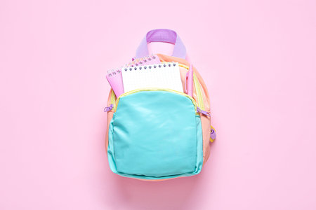 Color school backpack with stationery on pink background