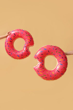 Women with swim rings in shape of donuts on beige background