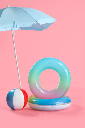 Swim rings with beach ball and umbrella on pink background