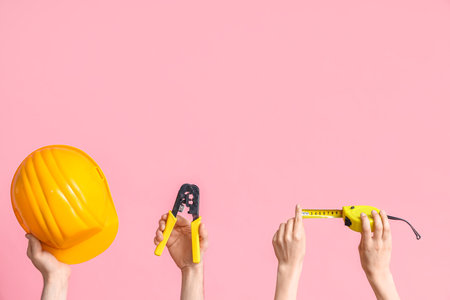 Electrician hands with tools and hardhat on pink backgroundの写真素材