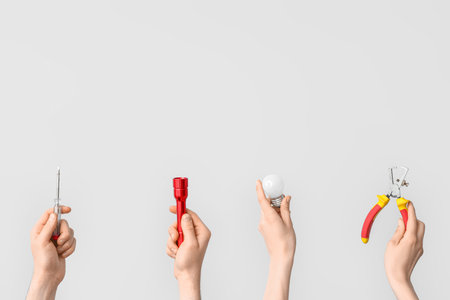Electrician hands with light bulb and tools on gray background