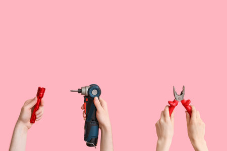 Electrician hands with tools on pink background