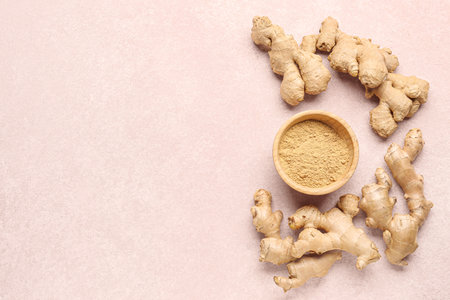 Fresh ginger roots and wooden bowl with dried powder on pink backgroundの写真素材