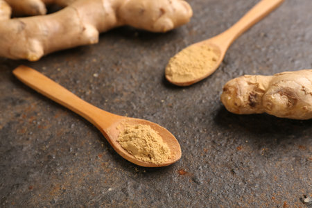 Fresh ginger roots and wooden spoons with dried powder on dark backgroundの写真素材
