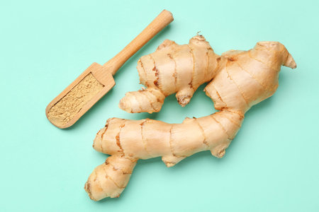 Fresh ginger root and wooden scoop with dried powder on turquoise background