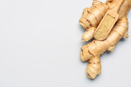 Fresh ginger root and wooden scoop with dried powder on gray background