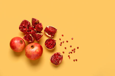 Fresh pomegranates and bowl with seeds on yellow backgroundの写真素材